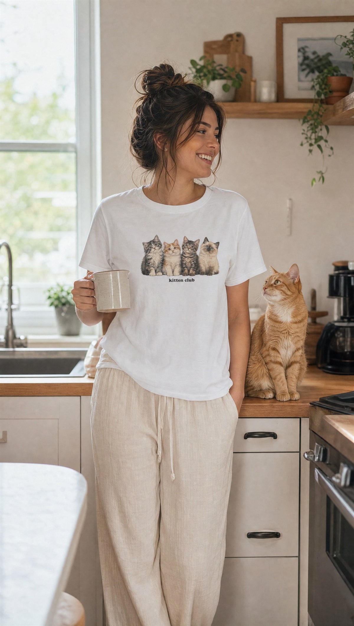 Kitten Club graphic tee with linen pants in a sunny kitchen, cat on the counter